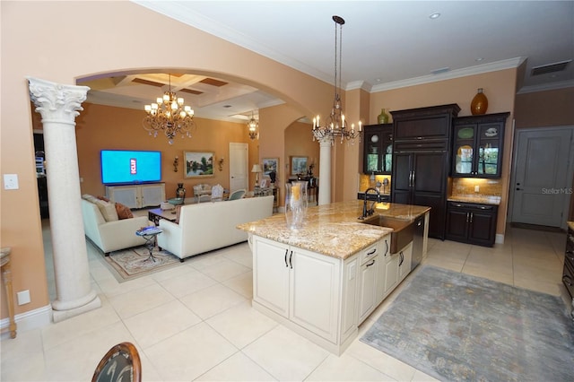 kitchen featuring sink, an island with sink, beamed ceiling, white cabinetry, and decorative columns