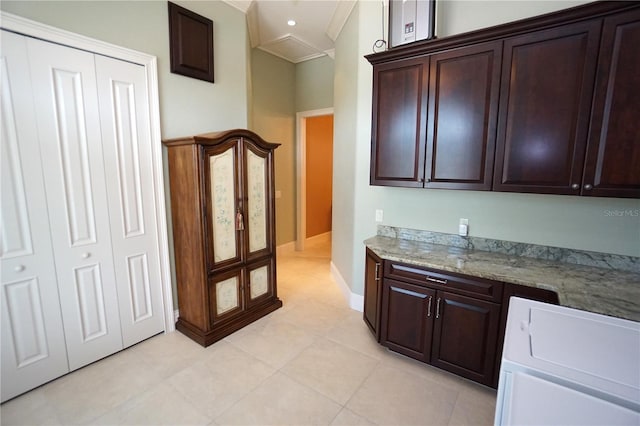 kitchen with light stone counters, crown molding, washer / dryer, dark brown cabinets, and light tile patterned flooring