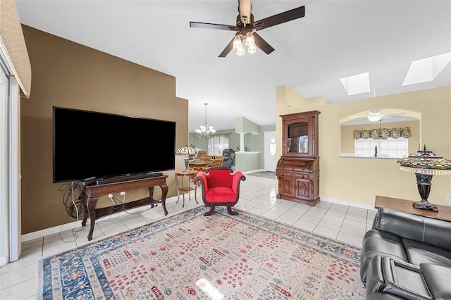 tiled living room featuring ceiling fan with notable chandelier and lofted ceiling with skylight