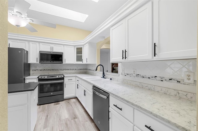 kitchen featuring sink, a skylight, appliances with stainless steel finishes, light hardwood / wood-style floors, and white cabinetry