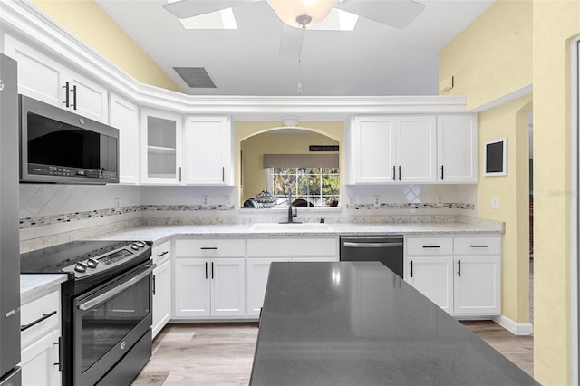 kitchen with appliances with stainless steel finishes, a skylight, white cabinetry, and sink