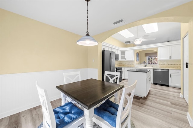 dining space featuring ceiling fan, light hardwood / wood-style floors, and a skylight