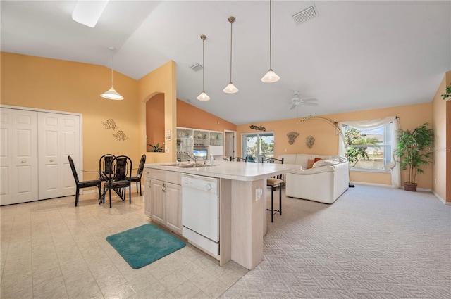 kitchen with a wealth of natural light, hanging light fixtures, white dishwasher, and an island with sink