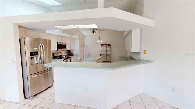 kitchen featuring kitchen peninsula, vaulted ceiling with skylight, light tile patterned floors, and stainless steel appliances