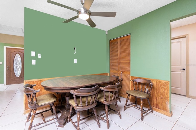 tiled dining space featuring wooden walls, a textured ceiling, and ceiling fan