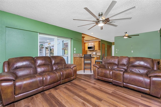 living room featuring light hardwood / wood-style floors, a textured ceiling, and ceiling fan