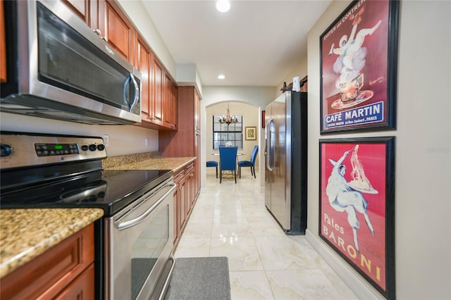 kitchen featuring arched walkways, brown cabinetry, appliances with stainless steel finishes, an inviting chandelier, and recessed lighting