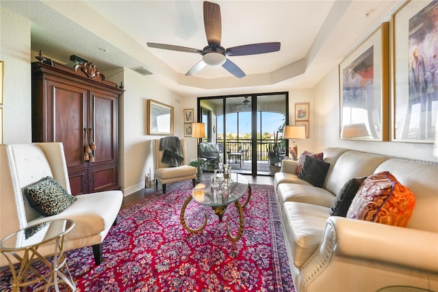 living area with baseboards, visible vents, ceiling fan, wood finished floors, and a tray ceiling