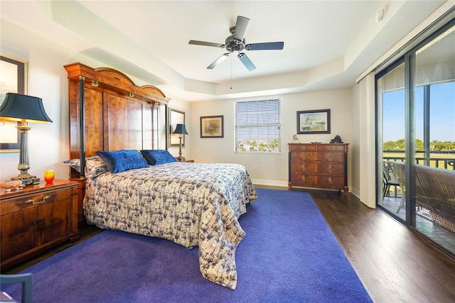 bedroom with dark wood-type flooring, ceiling fan, a tray ceiling, and access to outside