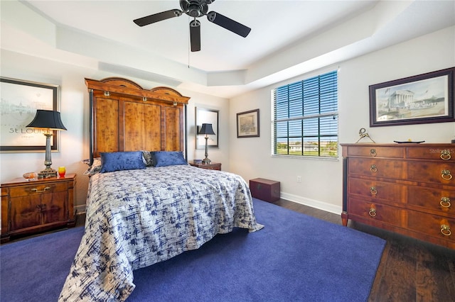 bedroom with ceiling fan, a raised ceiling, and dark hardwood / wood-style flooring