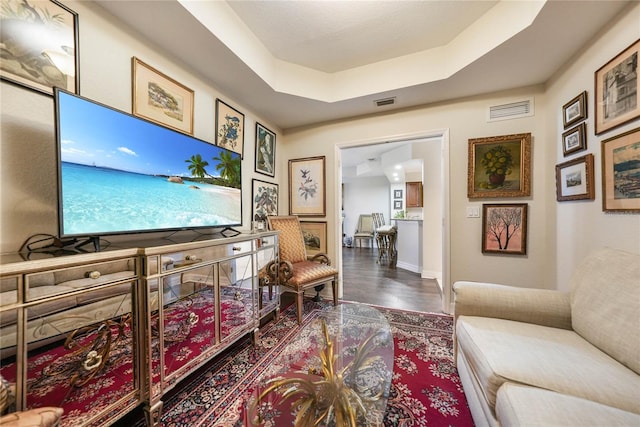 living area with baseboards, visible vents, a tray ceiling, and wood finished floors