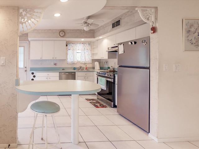 kitchen featuring appliances with stainless steel finishes, a kitchen bar, sink, white cabinets, and ceiling fan