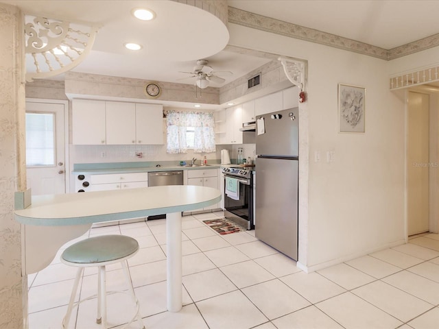 kitchen with stainless steel appliances, white cabinetry, light tile patterned floors, sink, and ceiling fan