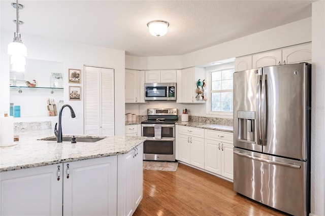 kitchen featuring stainless steel appliances, sink, light stone counters, decorative light fixtures, and white cabinets