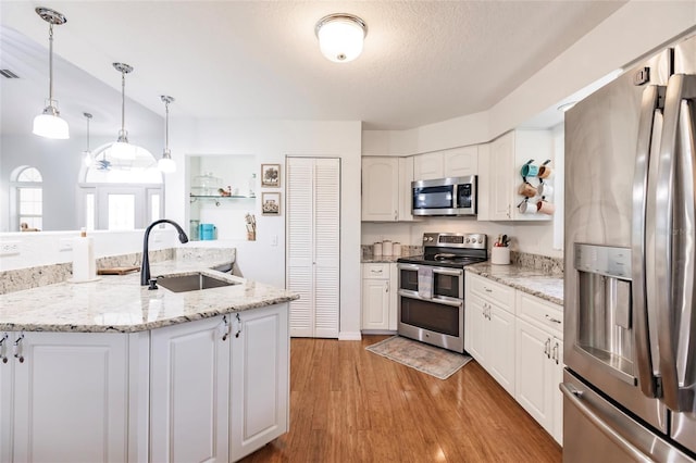 kitchen featuring white cabinetry, sink, appliances with stainless steel finishes, hanging light fixtures, and light hardwood / wood-style flooring