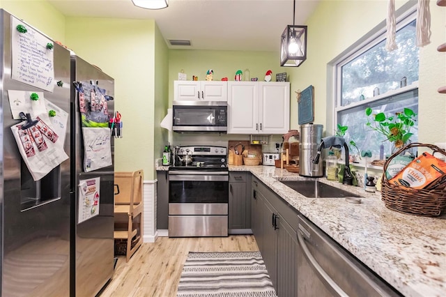 kitchen with stainless steel appliances, hanging light fixtures, sink, light hardwood / wood-style floors, and white cabinets