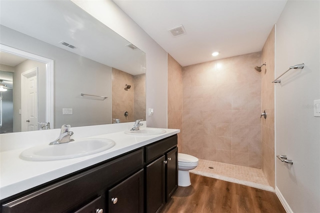 bathroom featuring toilet, vanity, hardwood / wood-style floors, and a tile shower