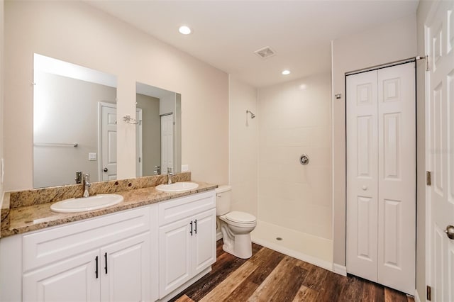 bathroom with a tile shower, vanity, hardwood / wood-style flooring, and toilet