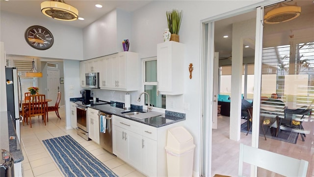 kitchen with stainless steel appliances, dark stone counters, light tile patterned floors, sink, and white cabinets