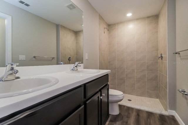 bathroom featuring toilet, vanity, wood-type flooring, and a tile shower