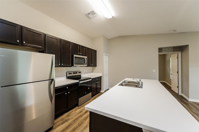 kitchen featuring light hardwood / wood-style floors, stainless steel appliances, vaulted ceiling, sink, and an island with sink