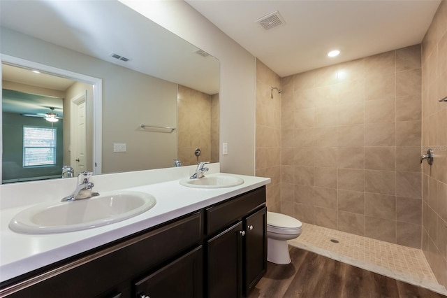 bathroom with wood-type flooring, a tile shower, vanity, toilet, and ceiling fan