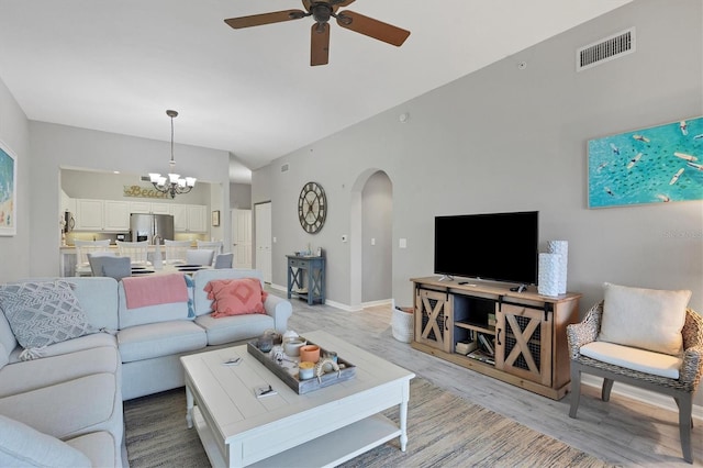 living room featuring ceiling fan with notable chandelier, lofted ceiling, and light hardwood / wood-style flooring