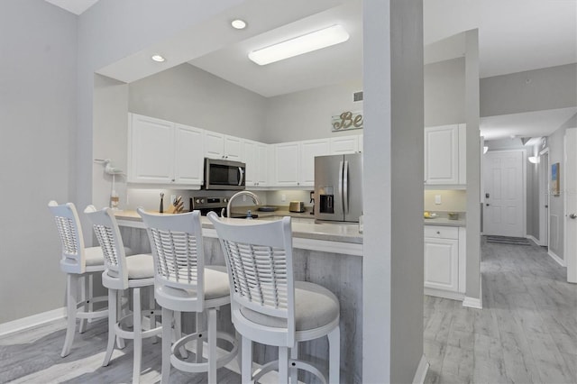 kitchen with kitchen peninsula, appliances with stainless steel finishes, a kitchen breakfast bar, light hardwood / wood-style flooring, and white cabinetry