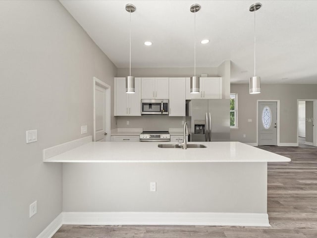 kitchen with white cabinets, appliances with stainless steel finishes, pendant lighting, and light hardwood / wood-style flooring