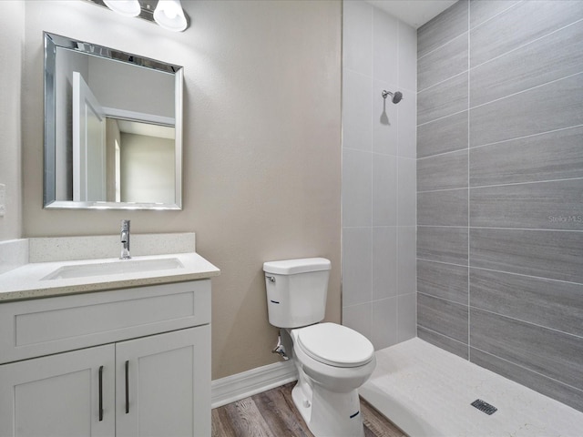 bathroom featuring wood-type flooring, vanity, toilet, and a tile shower