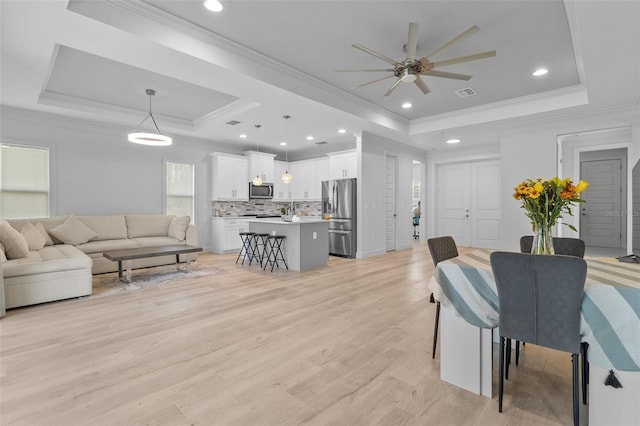 living room with ornamental molding, light hardwood / wood-style floors, ceiling fan, and a tray ceiling