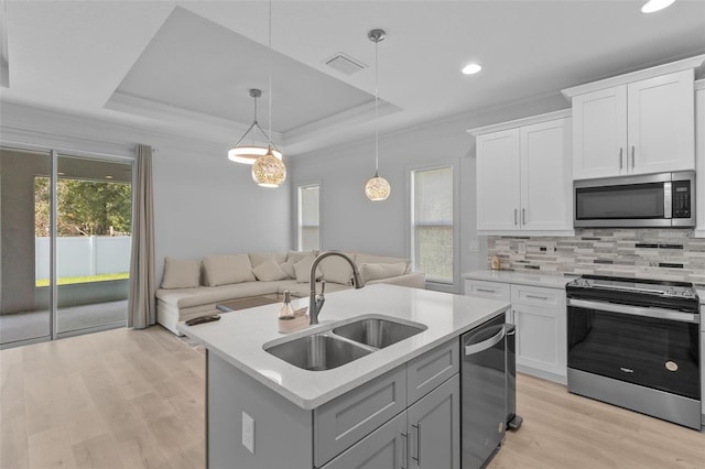 kitchen with white cabinets, appliances with stainless steel finishes, a kitchen island with sink, and sink