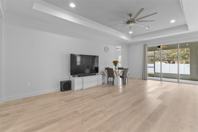 living room with light hardwood / wood-style floors, ceiling fan, ornamental molding, and a tray ceiling