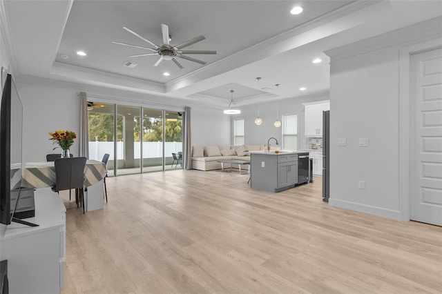 living room featuring light wood-type flooring, a tray ceiling, and sink