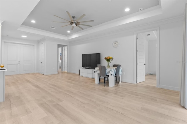 unfurnished living room featuring light wood-type flooring, crown molding, ceiling fan, and a raised ceiling