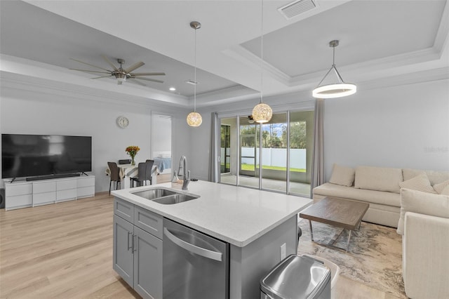 kitchen with hanging light fixtures, stainless steel dishwasher, a center island with sink, and a raised ceiling