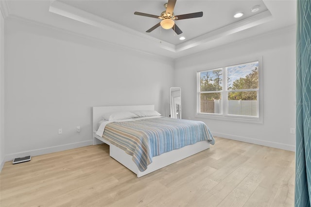 bedroom with light hardwood / wood-style floors, ornamental molding, a tray ceiling, and ceiling fan