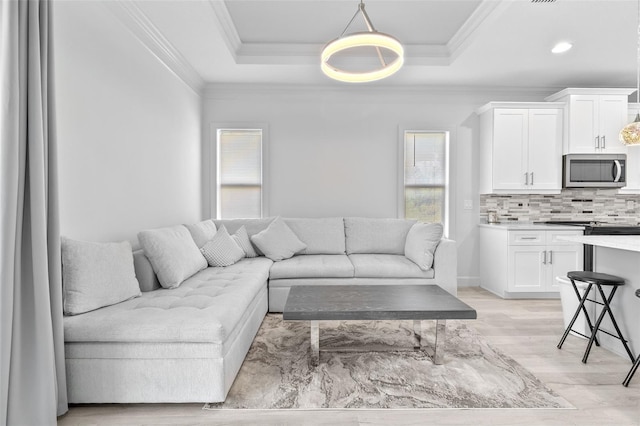 living room with light wood-type flooring, crown molding, and a tray ceiling