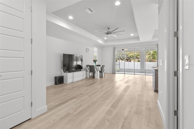 living room with light wood-type flooring, a tray ceiling, and ceiling fan