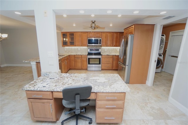 kitchen featuring a kitchen bar, tasteful backsplash, stainless steel appliances, built in desk, and stacked washer and dryer