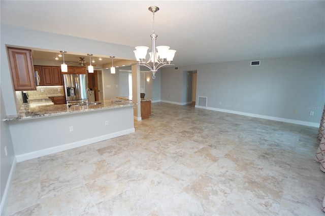 kitchen with kitchen peninsula, tasteful backsplash, decorative light fixtures, light stone counters, and stainless steel fridge with ice dispenser