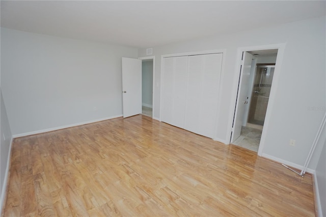 unfurnished bedroom featuring light hardwood / wood-style flooring, ensuite bath, and a closet