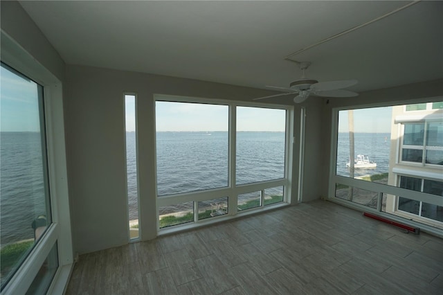 unfurnished sunroom with ceiling fan and a water view