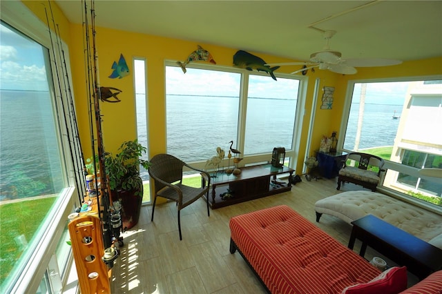 sunroom with ceiling fan and a water view