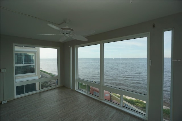 unfurnished sunroom with ceiling fan and a water view