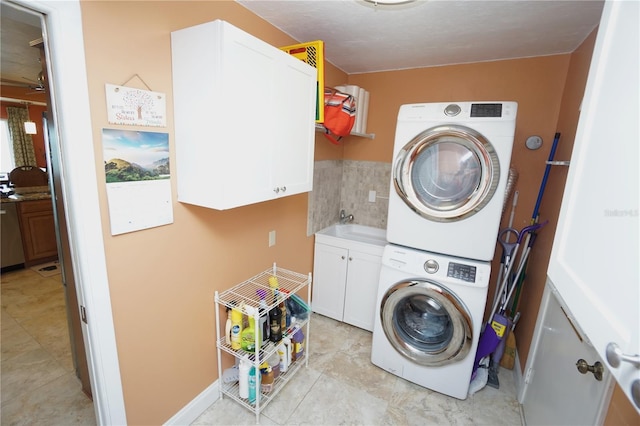 laundry area featuring stacked washer / dryer, sink, and cabinets