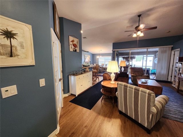 living room featuring light hardwood / wood-style floors, ceiling fan with notable chandelier, and vaulted ceiling