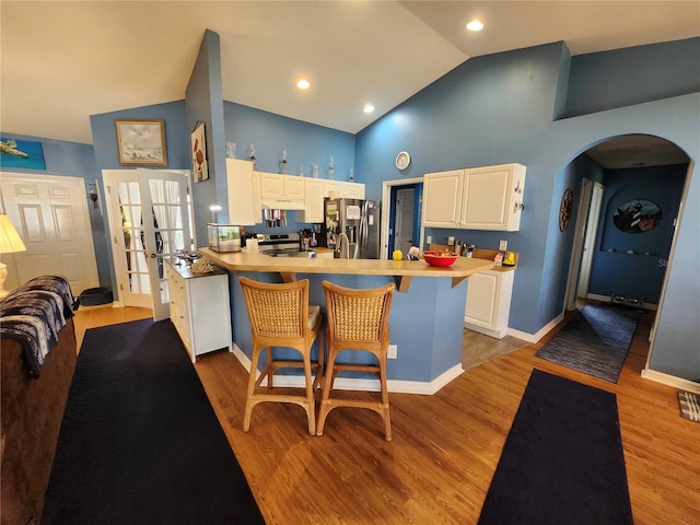 kitchen with stainless steel appliances, white cabinetry, a breakfast bar area, kitchen peninsula, and light hardwood / wood-style flooring