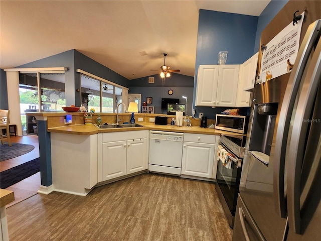 kitchen with stainless steel appliances, vaulted ceiling, kitchen peninsula, sink, and white cabinetry