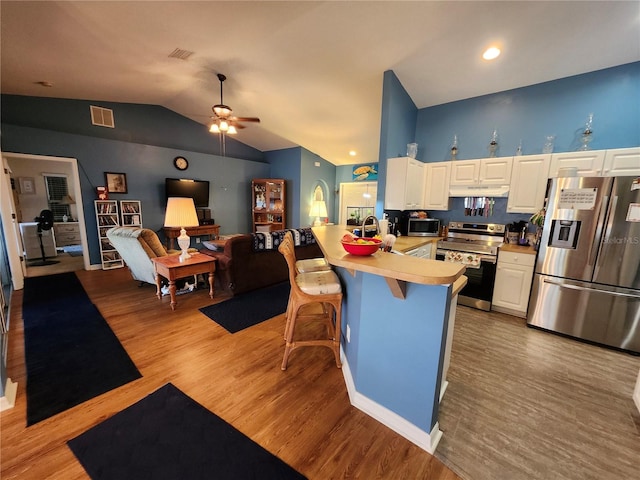 kitchen featuring appliances with stainless steel finishes, a kitchen breakfast bar, light hardwood / wood-style flooring, lofted ceiling, and white cabinets